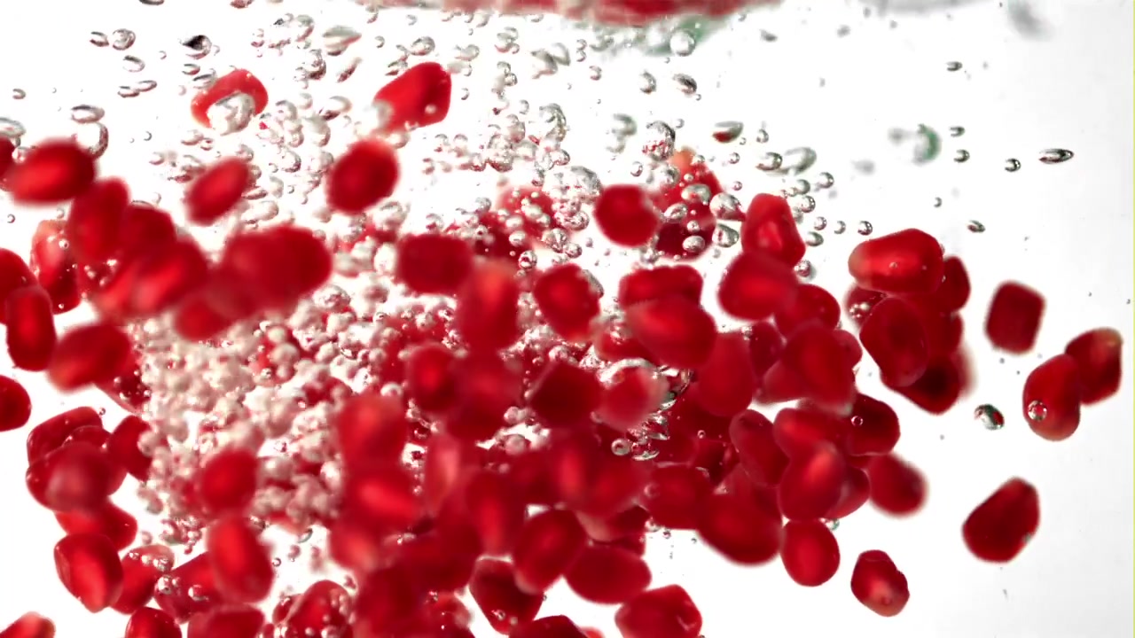 Red Pomegranate Seeds Falling into Water with Bubbles in Slow Motion