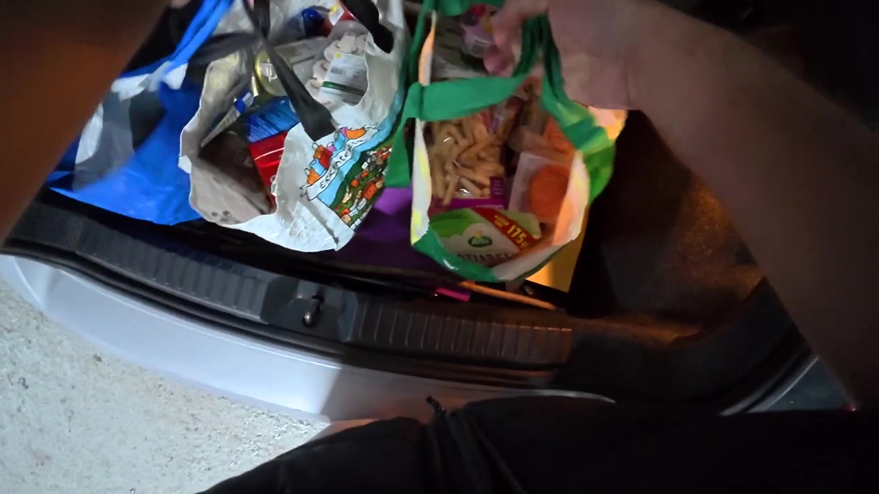 Person Unloading Groceries from Car Trunk in Parking Garage