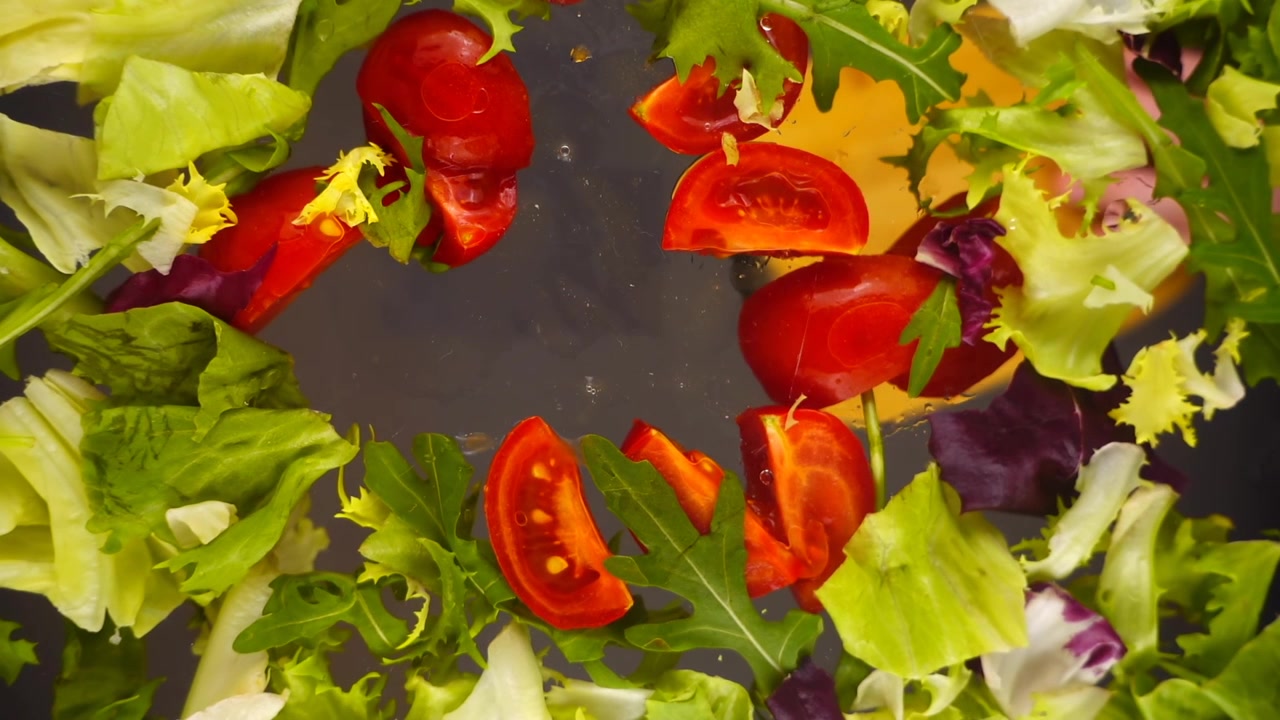 Preparazione di un'insalata con pomodori ed erbe aromatiche. Fette di pomodoro cadono in una ciotola di vetro. Movimento rallentato.