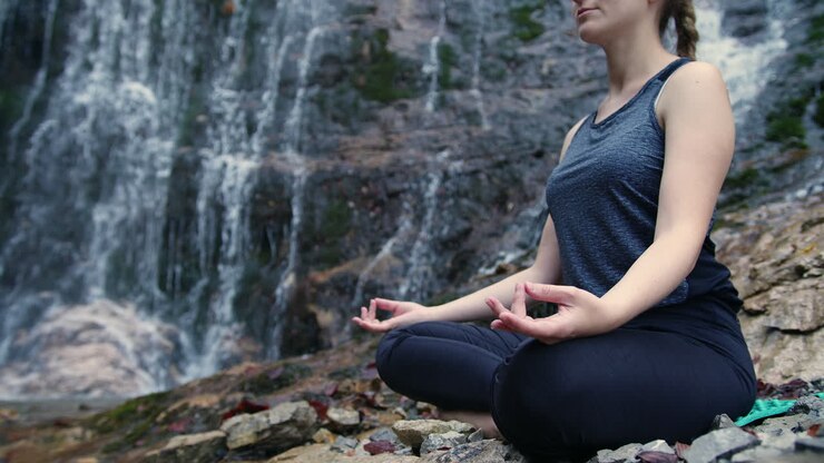 Chica practicando yoga flow junto a una cascada, meditando en posición de loto, grabado a mano.