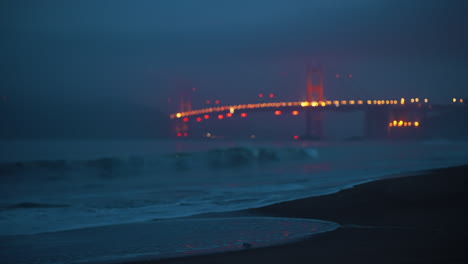 Morning-view-from-Baker-Beach-of-Golden-Gate-Bridge,-San-Francisco,-with-fog-and-dark-blue-clouds,-shot-cinematically