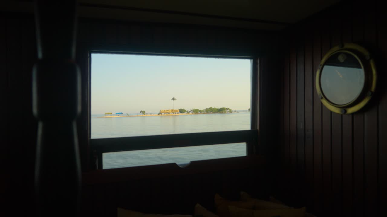 A remote tropical island is viewed through the window of a yacht that is passing by
