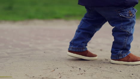 Cute-little-child-in-blue-jeans-walking-near-skateboard.-Baby-legs