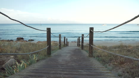 camino con listones de madera y cuerdas al lado que va a una playa tranquila al amanecer, mar mediterráneo