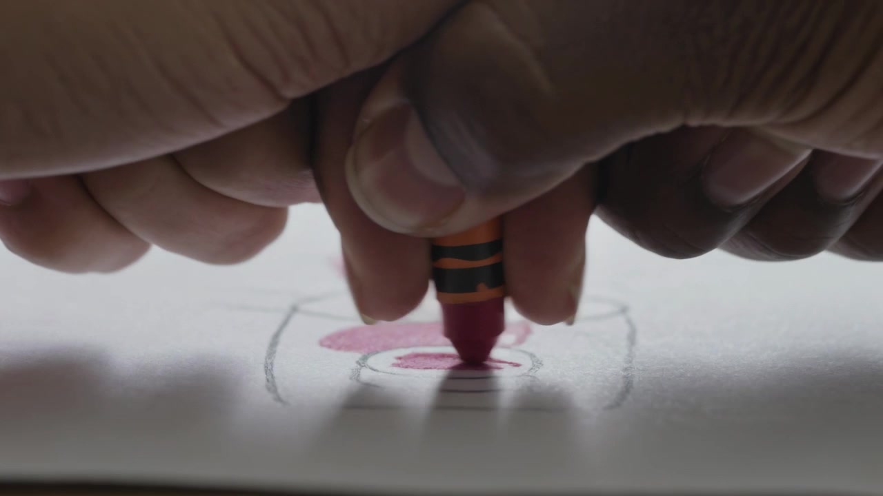 Touching red crayon tip, child's hands pressing, dragging on paper at table, filling oval