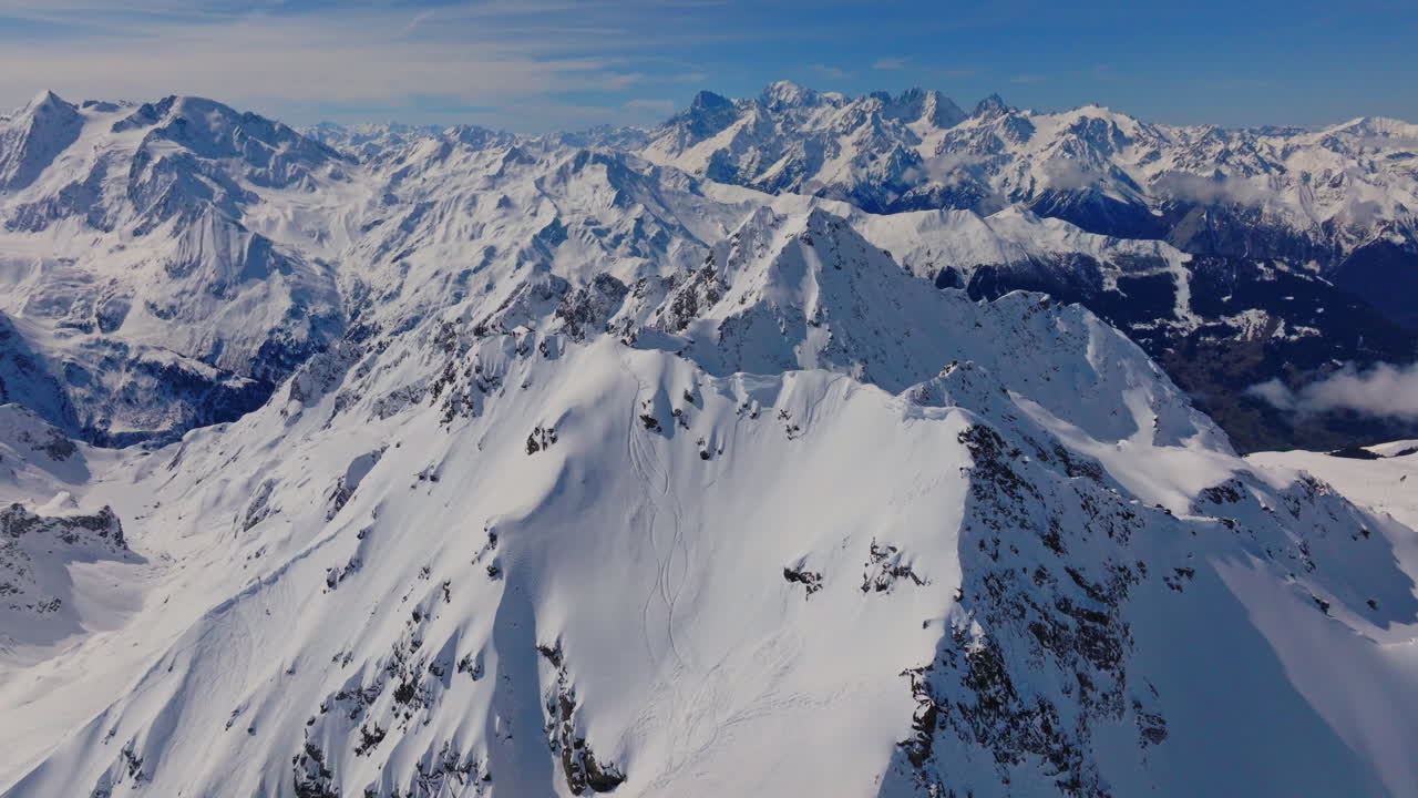 Riprese aeree dell'iconico paradiso del freeride di Verbier in una splendida giornata di sole. Cime innevate, ampi pendii aperti e leggendario terreno fuoripista sotto cieli alpini sereni