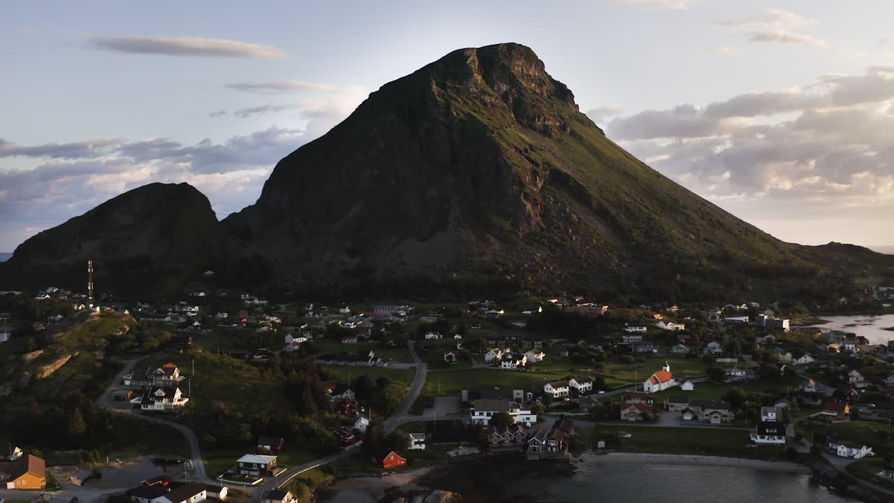 Aerial drone shot panning to the left showing the Island of Lovund with the summit of Lovundfjellet towering over the village. Lovund, Norway