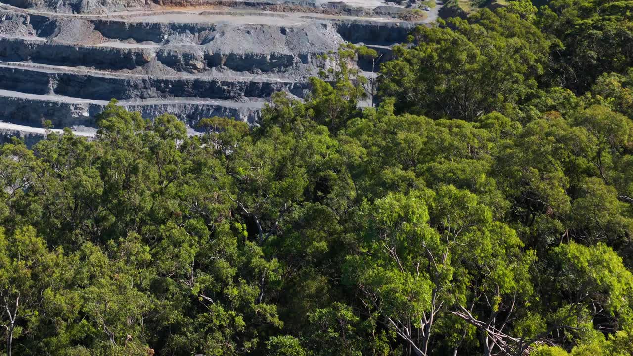 Aerial footage of a quarry surrounded by dense forest, showcasing contrasting natural and industrial landscapes under bright daylight