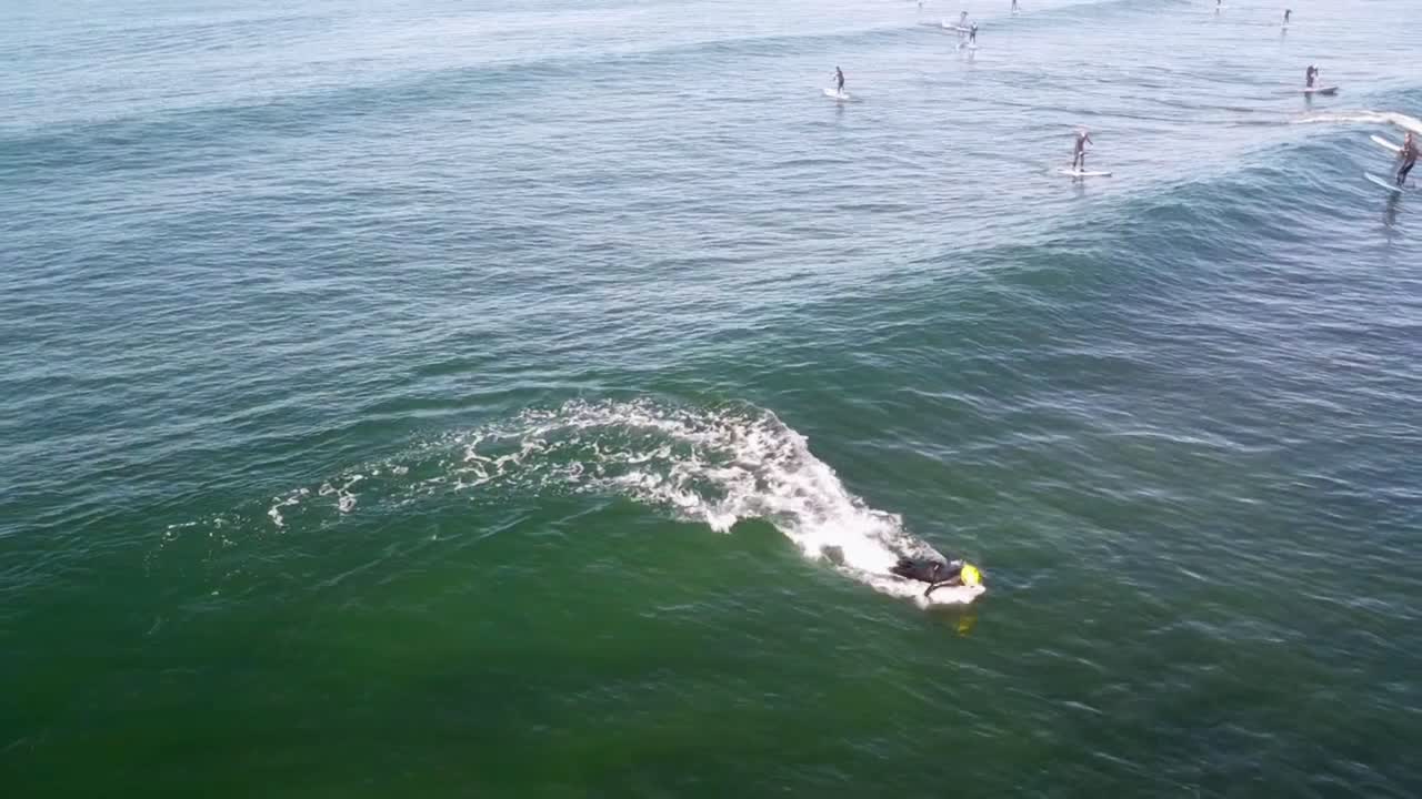 Surfer Riding a Wave with Paddleboarders in the Background