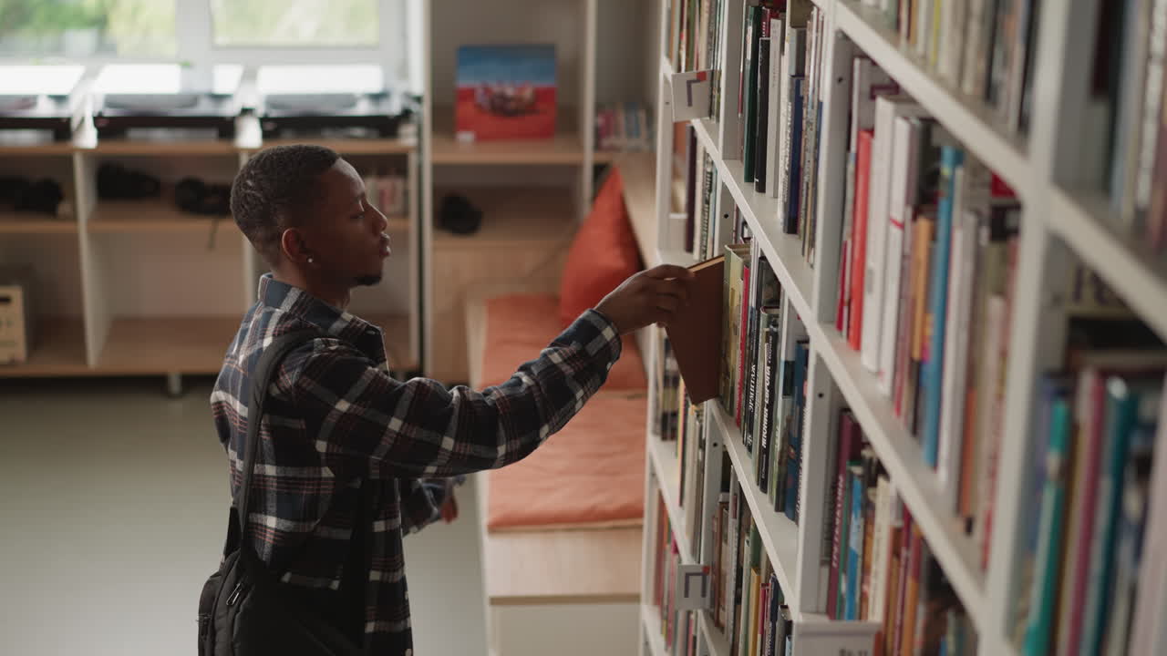 Dark-skinned guy scans shelf for book. African American student makes selections for individual task in university library. Man explores offerings in bookstore