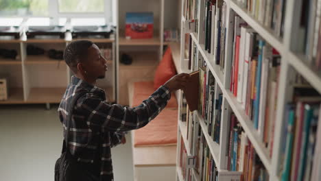 dark-skinned guy scans shelf for book. african american student makes selections for individual task in university library. man explores offerings in bookstore