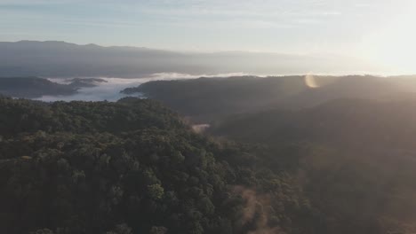 Aerial-view-of-a-lake-nestled-amidst-mountains-during-sunset,-with-some-fog-appearing-over-the-lake-between-the-green-mountains-in-Colombia