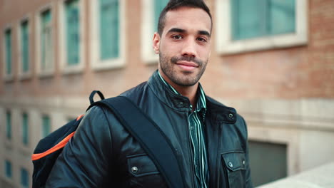 young man with backpack standing and smiling at camera outdoors.