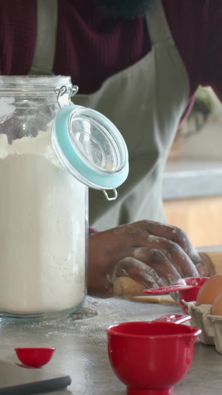 Vídeo vertical: Cozinheiro de avental preparando-se para assar, moldando massa na cozinha com um rolo.
