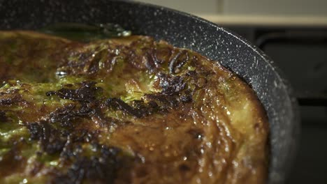 acercamiento extremo en una hermosa toma de una auténtica frittata italiana cocinada en una sartén grande con grasa burbujeante proveniente de los lados