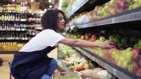 curly female arranging big green apples on shelf