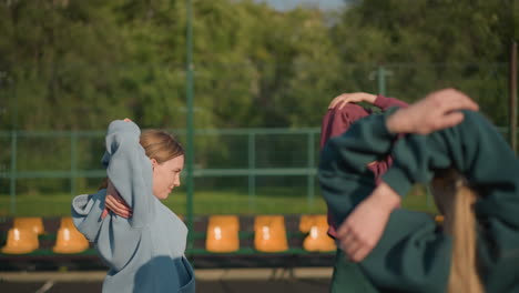 joven atleta con traje deportivo realizando ejercicios de acondicionamiento físico con una sonrisa cálida, el fondo presenta un campo abierto y asientos, creando una atmósfera enérgica y motivadora