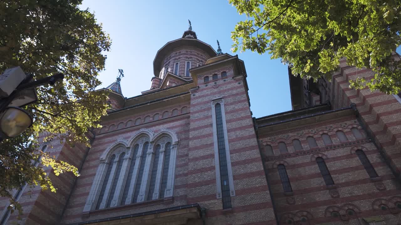 Tilt-up footage of the Metropolitan Cathedral in Timisoara, Romania, with trees in the foreground adding depth and natural framing