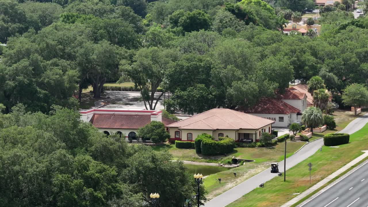 The Villages sign displayed on a decorative overpass along a major roadway near Spanish Springs, Florida. The road is lined with greenery and light traffic. Aerial.
