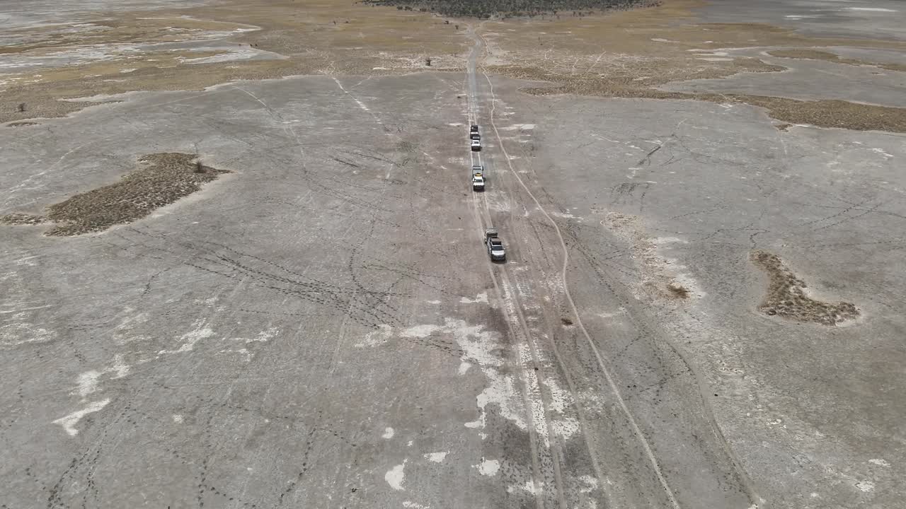 Convoy of off-road trucks drives across rugged, barren plains, aerial
