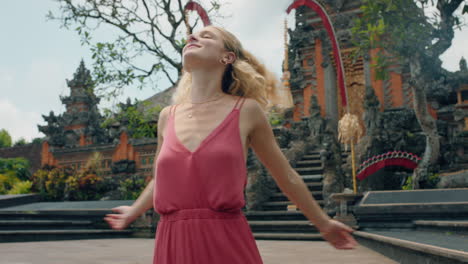 Glückliche-Frau-Tanzt-Im-Saraswati-Tempel-Und-Feiert-Reisen-Und-Genießt-Die-Kultur-Balis,-Indonesiens-4k