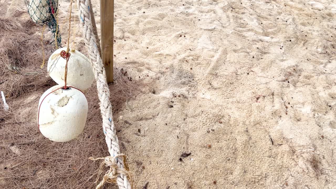 Primo piano di galleggianti da pesca bianchi abbandonati e corda usurata adagiati sulla sabbia di una spiaggia tropicale