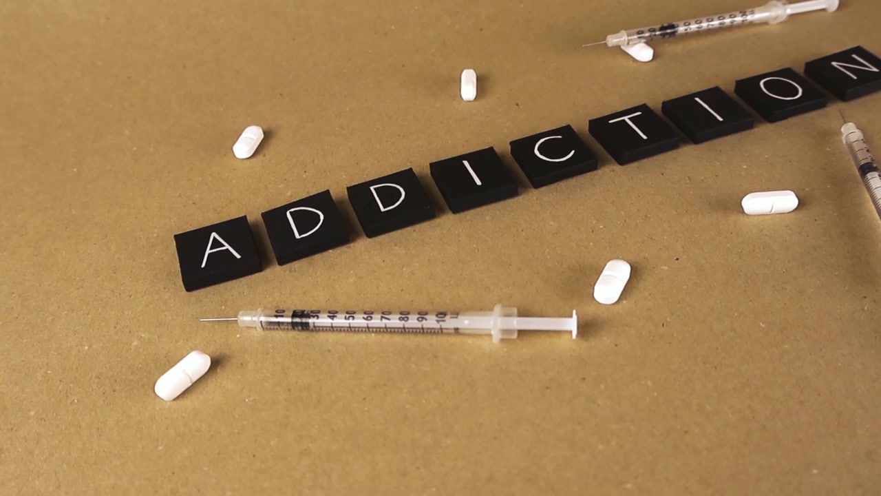 Vídeo conceitual mostrando a palavra "vício" cercada por seringas com agulhas e pílulas brancas, representando os perigos do abuso de drogas, dependência e a crise de opioides