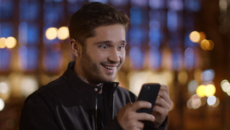 Joyful-man-reading-message-on-mobile-phone-outdoors.-Guy-looking-phone-screen