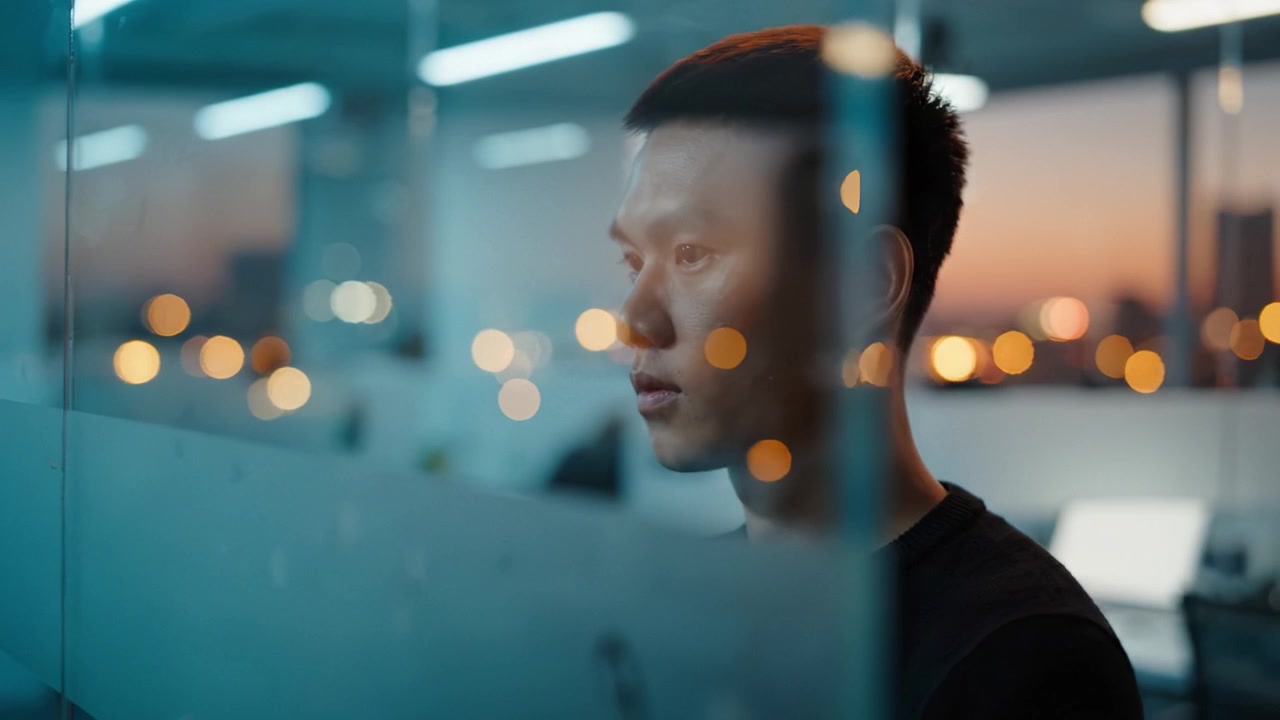 Contemplative Profile of a Young Man Gazing Outward Through Glass, Capturing a Moment of Reflection and Serene Focus Against a Calm Urban Twilight Setting