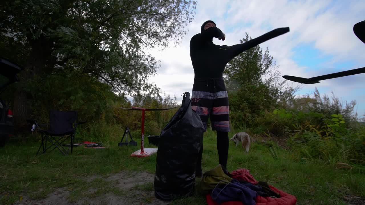 el surfista se está poniendo su neopreno de traje de neopreno junto a su tabla de aluminio
