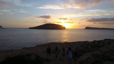 aerial shot of friends on cliffs watching sun set over sea