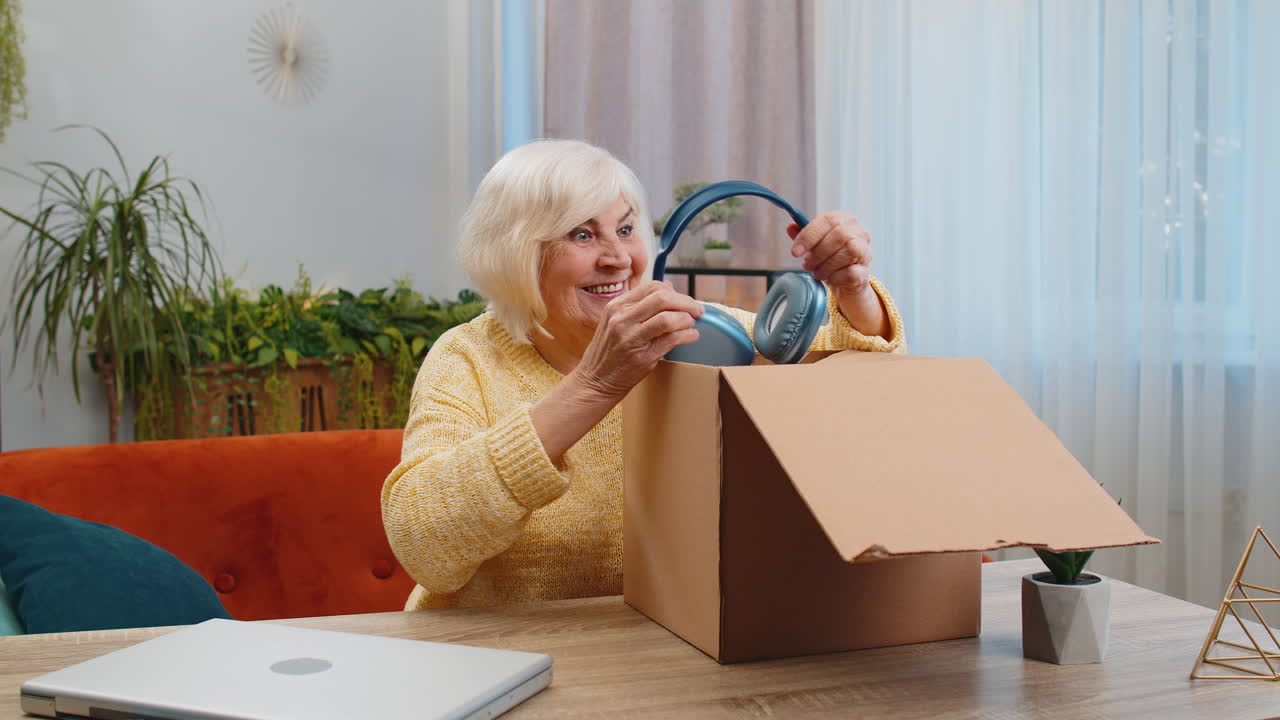 Happy senior woman shopper unpack headphones cardboard box delivery parcel online shopping purchase