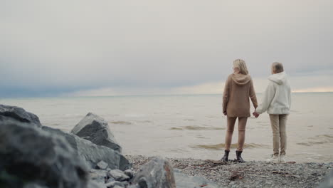 a mother with a teenage daughter stands on a rocky seashore. relationships and family concept