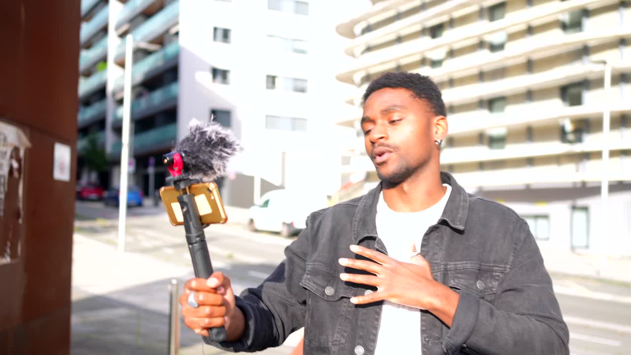 Young man vlogging with smartphone and microphone on a city street