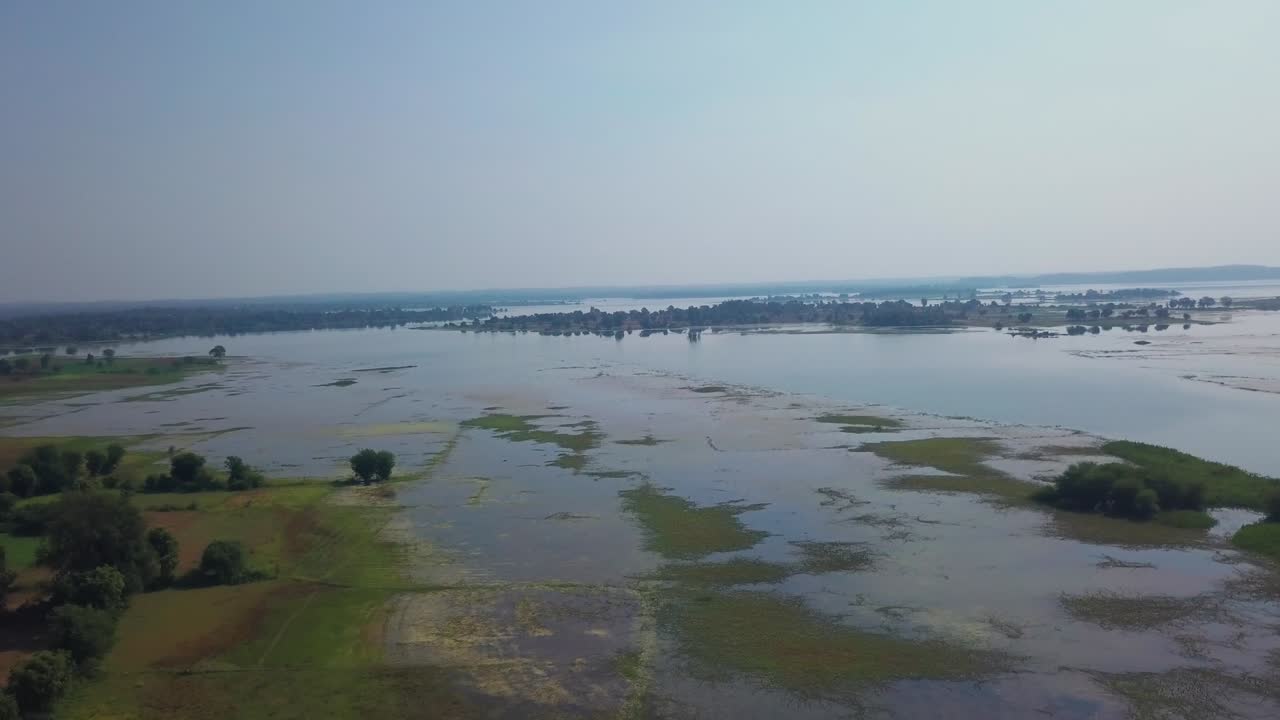 Zone umide nel Gujarat, India, che mostrano pozze d'acqua poco profonde, chiazze di vegetazione verde e alberi sparsi dopo la stagione dei monsoni. Una lenta ripresa aerea in avanti rivela il vasto paesaggio allagato