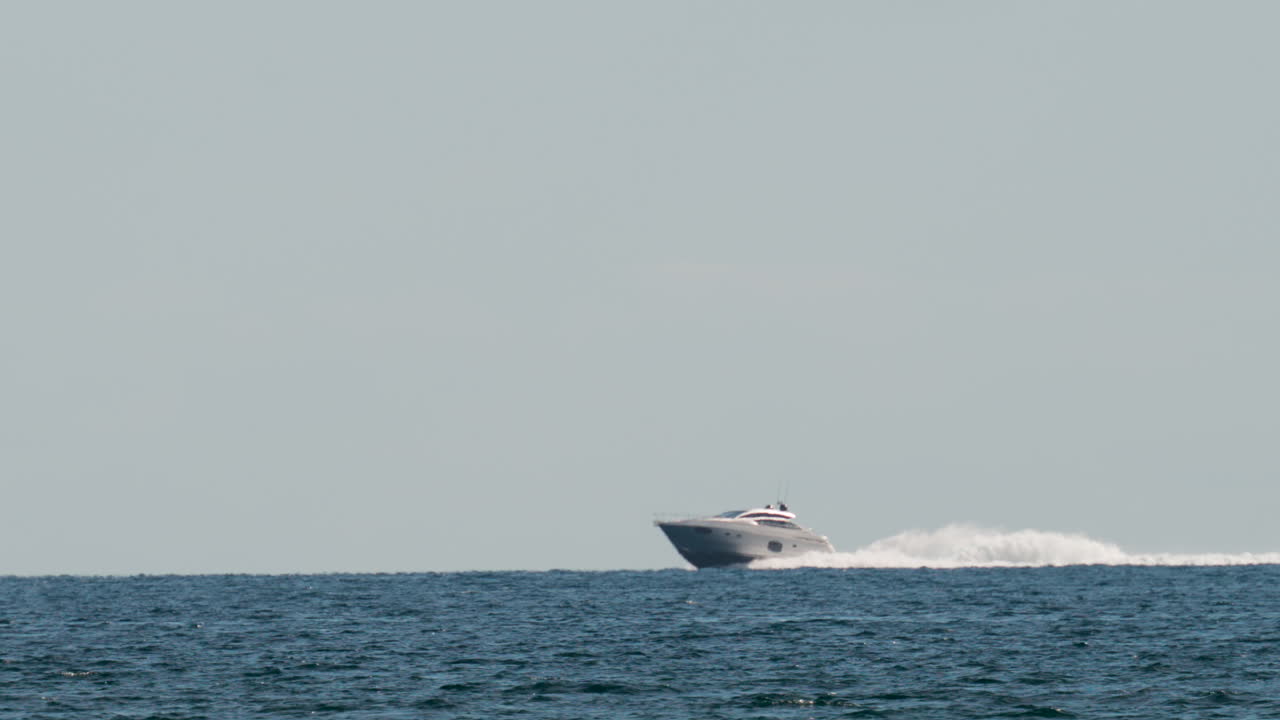A luxury speedboat racing across open blue water under a clear sky, leaving a long white wake