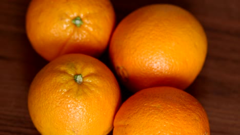 four ripe juicy oranges on a brown wooden surface.