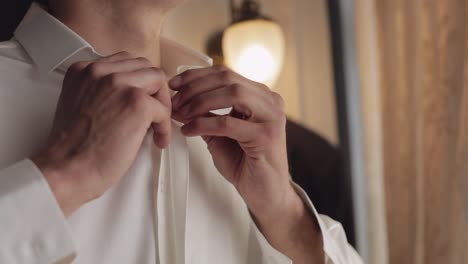 hombre elegante en chaqueta sujeta los botones, abotonando camisa blanca preparándose para salir cerca de la ventana