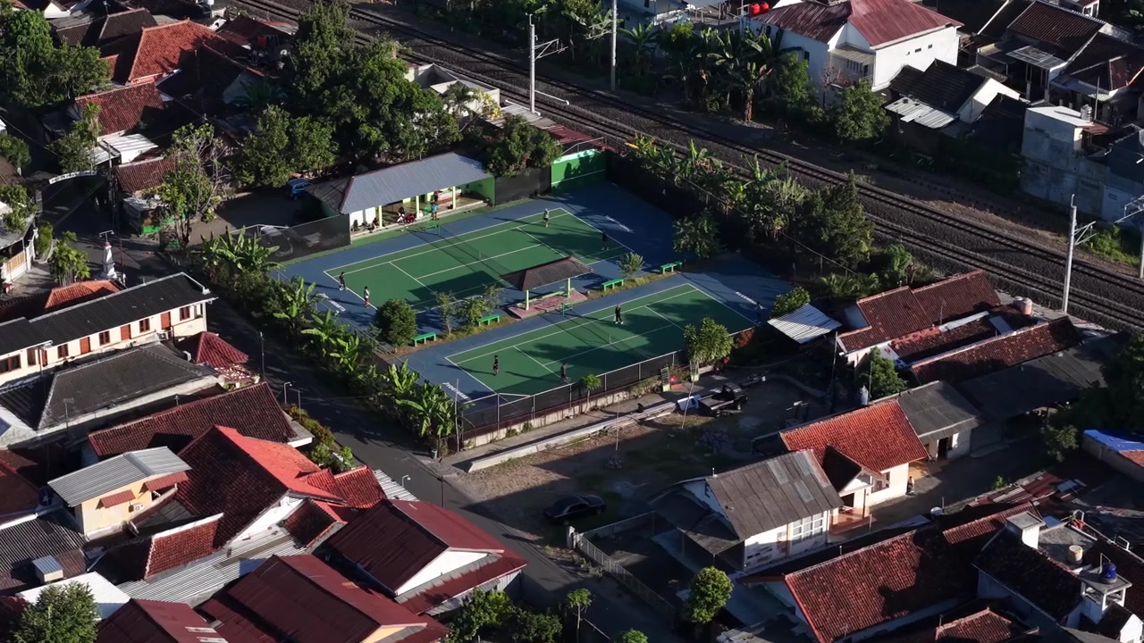 Morgenluftfoto af en tennisbane mellem et byområde og kanten af en jernbanelinje i Yogyakarta, Indonesien.