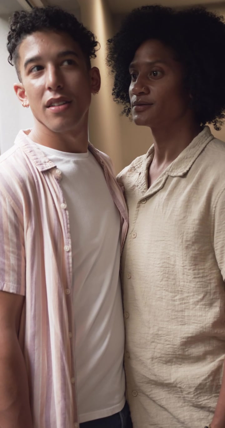 La luce del giorno cattura lo sguardo, l'uomo a sinistra sposta lo sguardo, l'uomo a destra in piedi vicino all'ingresso con camicia rosa e braccialetto.