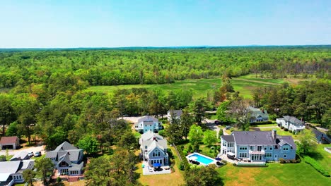 high-quality aerial drone video of a cozy cottage-style house in a suburban setting, featuring an expansive back porch, comfortable patio furniture, and shaded by towering, vibrant green trees.