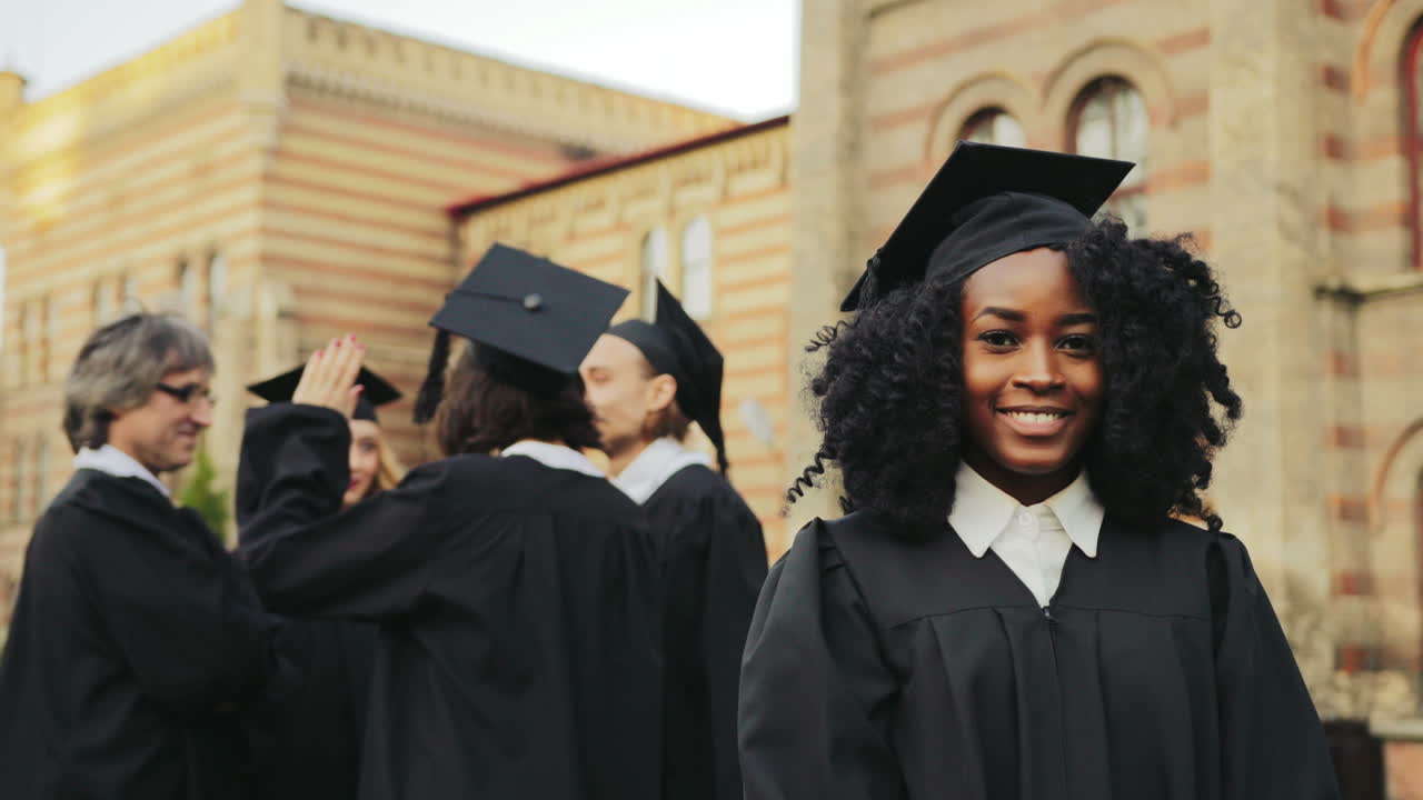 Portrait of the African American smiled young graduated woman posing to the camera and smiling in front of the University