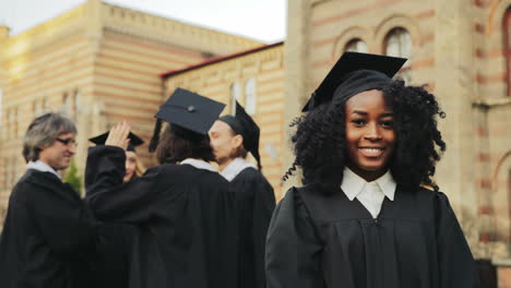 retrato de la joven graduada afroamericana sonriente posando para la cámara y sonriendo frente a la universidad