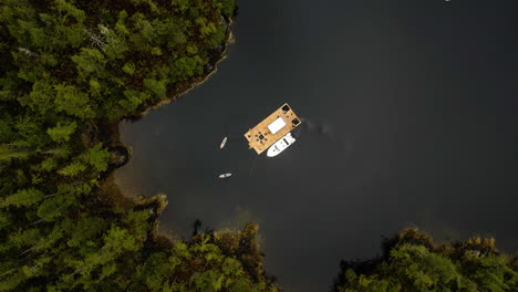 Aerial-riser-above-wood-fired-floating-sauna-with-people-on-SUP,-Tofino,-BC