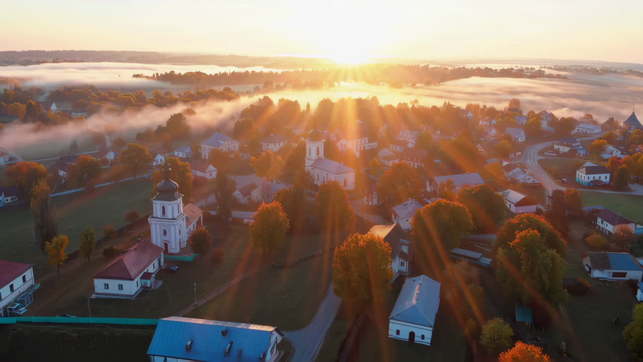 Aerial View of a Village with Church and Autumn Trees During a Misty Sunrise