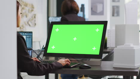 cad specialist using computer with greenscreen at office desk