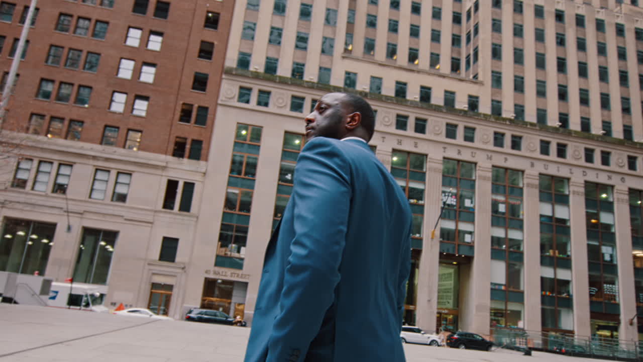 New York, USA, 28 maggio 2025: Uomo d'affari in abito blu che guarda i grattacieli di New York. Vista dal basso di un uomo americano in piedi nel distretto finanziario di Lower Manhattan, circondato da edifici alti.