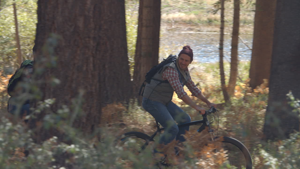 Casal conversando enquanto pedala em bicicletas de montanha na floresta, em panorâmica fechada