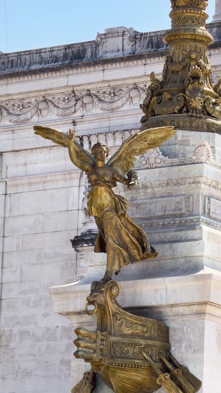 Primo piano di statua alata dorata su facciata di monumento ornato in piena luce diurna.