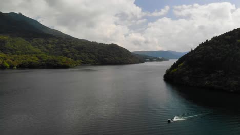 flying aerial drone shot over beautiful lake with forest hills and blue, cloudy sky and speedboat